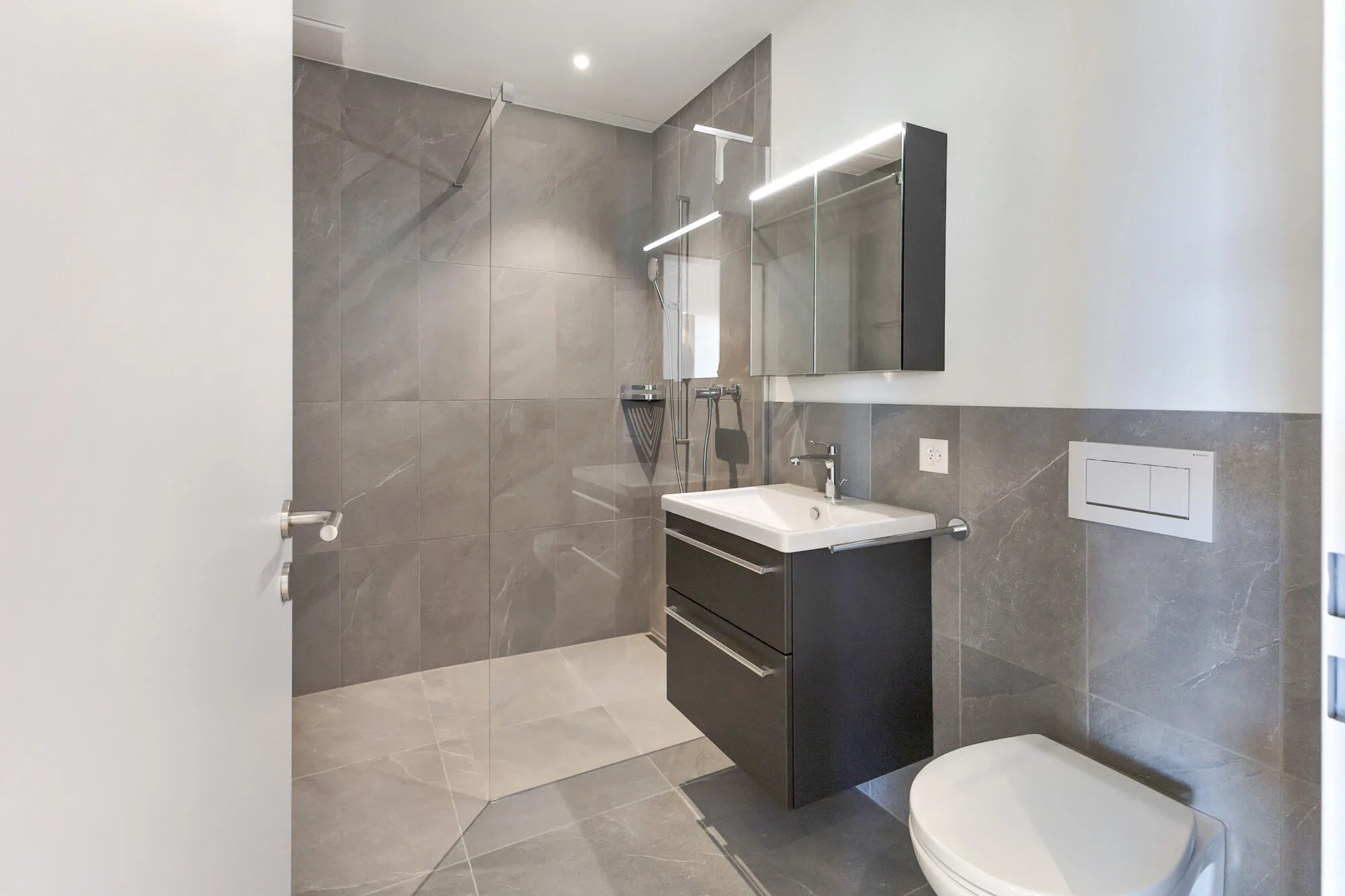 Modernes, graues Badezimmer mit Dusche und Waschbecken.