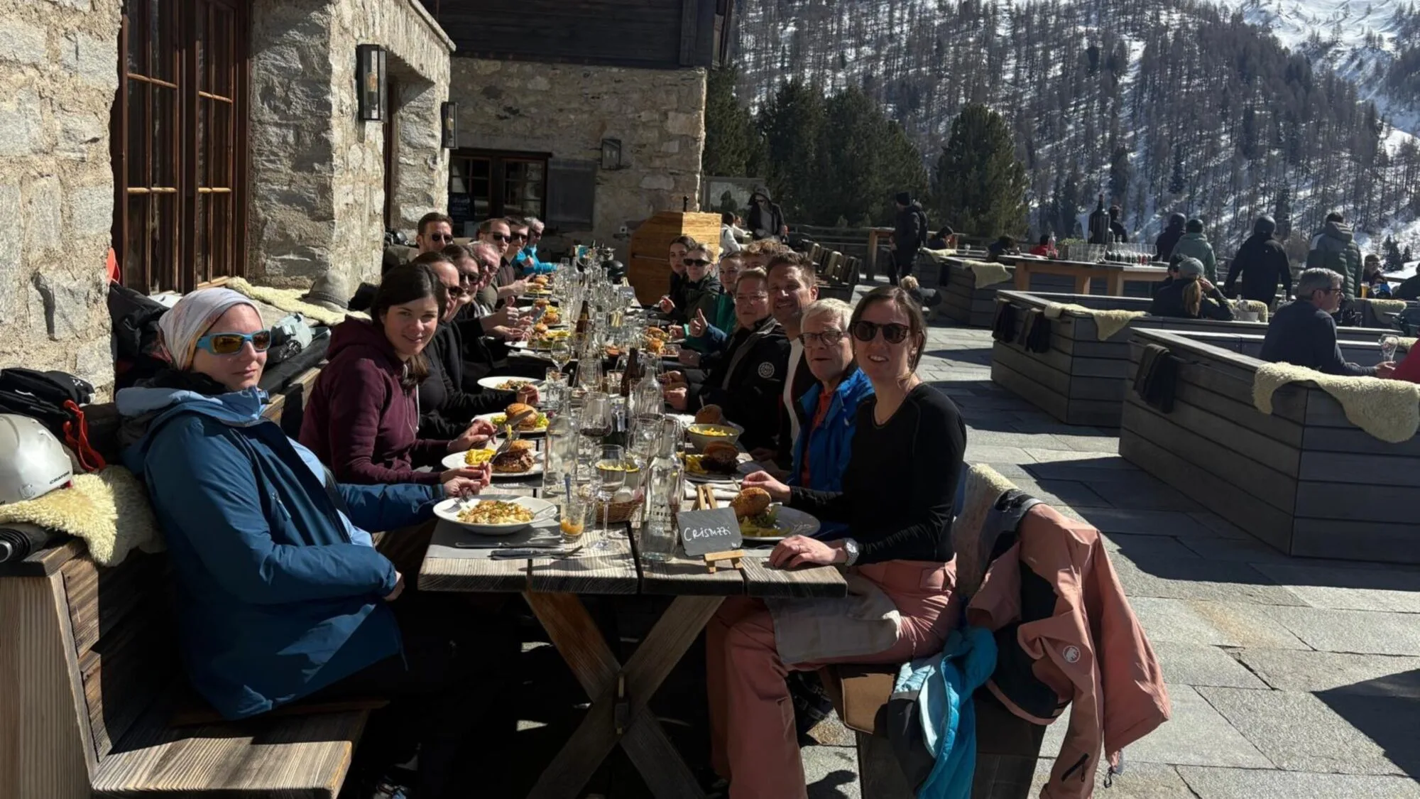Gruppe speist draußen im Schnee, Sonne scheint.